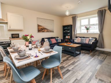 A dining table set with dishes and glasses next to a living area with sofas and a coffee table at Lonnon Cottage in Alnmouth