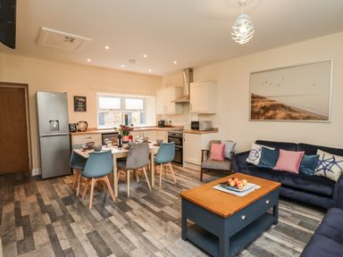 An open plan kitchen and living room with a dining table set for six and blue and grey chairs at Lonnon Cottage in Alnmouth