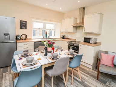A kitchen and dining area with a dining table set for six and modern appliances at Lonnon Cottage in Alnmouth