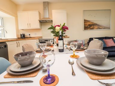 A dining table set with bowls plates glasses and cutlery in a kitchen area with cabinets and a stove at Lonnon Cottage in Alnmouth