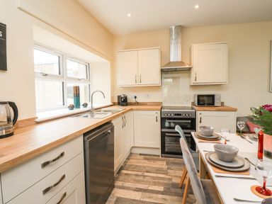 A kitchen with wooden countertops, white cabinets, a dishwasher, stove, microwave, dining table, and chairs at Lonnon Cottage in Alnmouth