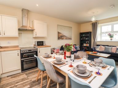A kitchen and dining area with a table set for six and a living room with sofas and a bookshelf at Lonnon Cottage in Alnmouth