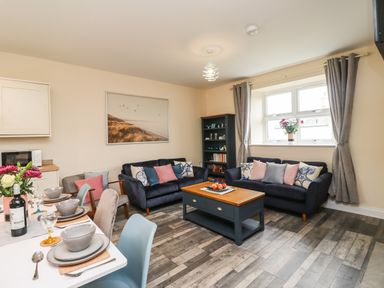 A living room with two sofas and a coffee table near a window with curtains at Lonnon Cottage in Alnmouth
