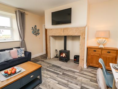 A living room with a wood stove fireplace a blue sofa a wooden coffee table and a wooden cabinet at Lonnon Cottage in Alnmouth