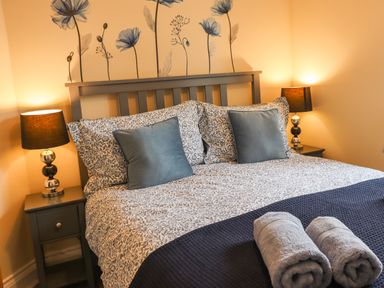 A bedroom with a double bed two bedside tables with lamps and rolled towels on the bed at Lonnon Cottage in Alnmouth