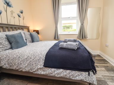 A bedroom with a bed made with floral bedspread and blue pillows and towels on the foot of the bed at Lonnon Cottage in Alnmouth