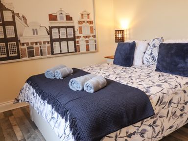A bedroom with a bed covered with floral bedding navy throw pillows and rolled towels on the bed at Lonnon Cottage in Alnmouth