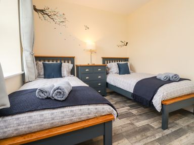 A bedroom with two single beds with pillows and towels separated by a chest of drawers and a lamp and bird wall decals at Lonnon Cottage in Alnmouth