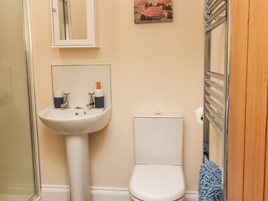 A bathroom with a pedestal sink, toilet, wall-mounted mirror cabinet, chrome towel rail with blue towel and shower enclosure at Lonnon Cottage in Alnmouth