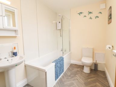 A bathroom with a bathtub shower combination a toilet a sink and turtle wall decals at Lonnon Cottage in Alnmouth