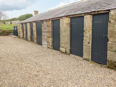 A row of stone storage units with dark wooden doors on a gravel ground at Lonnon Cottage in Alnmouth