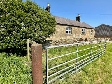 A stone house with two chimneys behind a metal gate and grassy area at Lonnon Cottage in Alnmouth