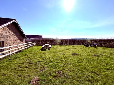 A fenced grassy yard with a wooden picnic table and two chairs at Lonnon Cottage in Alnmouth