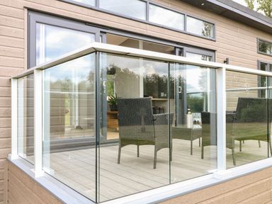 A patio with glass railing and outdoor chairs and a table with wine glasses at Willow Lodge in Winthorpe near Newark-On-Trent