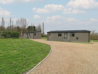 Two single-story rectangular buildings with beige siding on a gravel driveway surrounded by grass and trees at Willow Lodge in Winthorpe near Newark-On-Trent