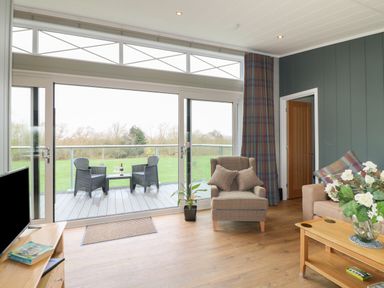 A living room with armchairs a sofa a coffee table and sliding glass doors opening to a balcony at Willow Lodge in Winthorpe near Newark-On-Trent
