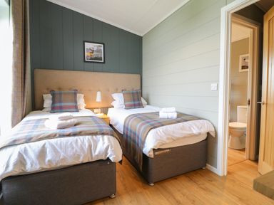 A bedroom with two single beds a nightstand with a lamp and an open door showing a bathroom at Willow Lodge in Winthorpe near Newark-On-Trent