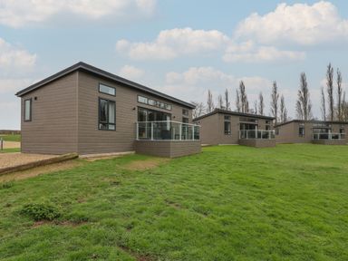 Three modern single-story lodges with glass balconies on a grassy area at Willow Lodge in Winthorpe near Newark-On-Trent