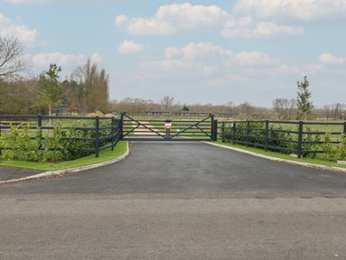 A black metal gate across a paved driveway with green hedges on both sides and fields in the background at Willow Lodge in Winthorpe near Newark-On-Trent