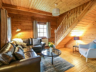 A living room with a leather sofa a round glass coffee table a gray armchair and wooden stairs at Moyle Lodge in Dalbeattie