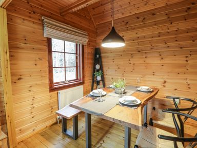 A dining area with a wooden table set for four people two chairs and a bench a window and a shelf at Moyle Lodge in Dalbeattie