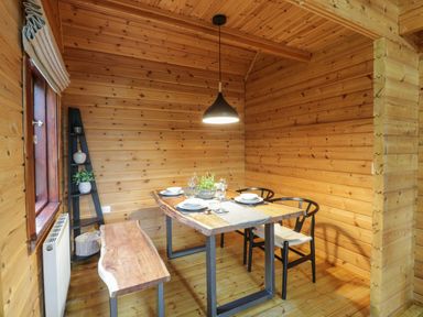 A dining area with wooden walls a wooden table set with plates and glasses two black chairs and a wooden bench at Moyle Lodge in Dalbeattie