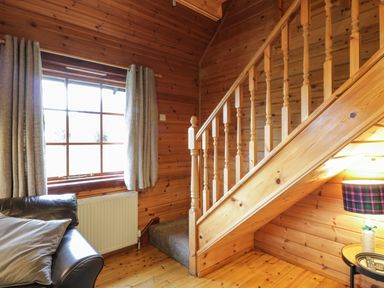 A wooden interior room with a staircase a window with curtains a sofa and a lamp at Moyle Lodge in Dalbeattie