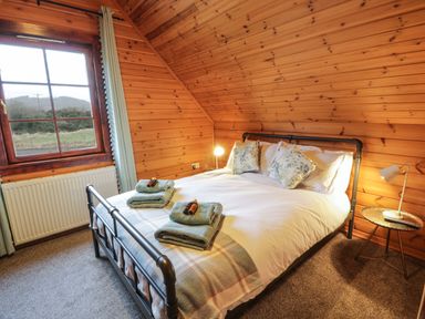 A bedroom with a double bed folded towels on the bed and a side table with a lamp at Moyle Lodge in Dalbeattie