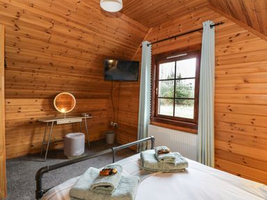 A bedroom with wooden walls a bed with folded towels a dressing table with a round mirror a wall-mounted television and a window with curtains at Moyle Lodge in Dalbeattie