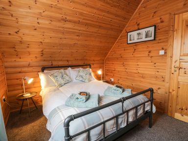 A bedroom with a bed and folded towels on it and wooden panel walls at Moyle Lodge in Dalbeattie