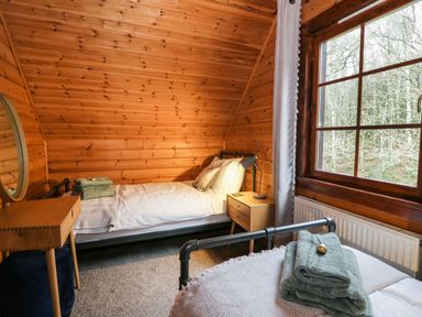A bedroom with wooden walls two single beds bedside table lamp window and folded towels at Moyle Lodge in Dalbeattie