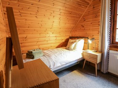 A bedroom with a single bed bedside table with a lamp folded towels and wooden walls and ceiling at Moyle Lodge in Dalbeattie