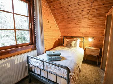 A small bedroom with a single bed towels on the bed a bedside table with a lamp and a window at Moyle Lodge in Dalbeattie