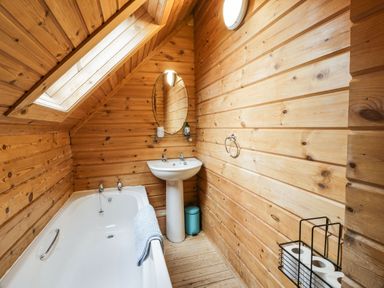 A bathroom with wooden walls a bathtub a pedestal sink an oval mirror and toilet paper rolls at Moyle Lodge in Dalbeattie