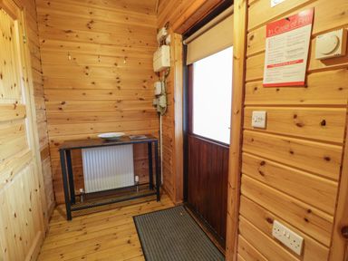 A wooden entrance hallway with a door mat a table with a bowl and a radiator behind it at Moyle Lodge in Dalbeattie