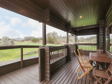 A covered wooden porch with a table and chairs overlooking a grassy outdoor area at Moyle Lodge in Dalbeattie