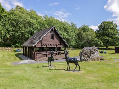 A wooden cabin with two metal deer sculptures on a lawn near trees at Moyle Lodge in Dalbeattie