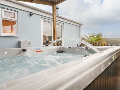 An outdoor hot tub with water jets near a light blue house with windows and a sliding door at The View in Cardinham