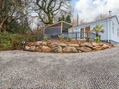 A small light blue house with a covered porch and a fenced garden on a gravel driveway at The View in Cardinham