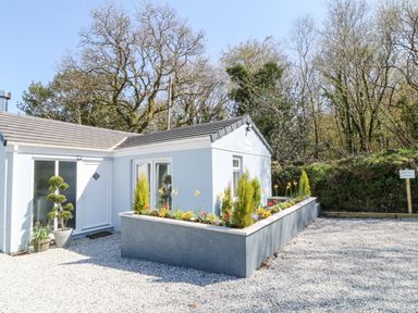 A white single story house with a triangular roof and rectangular flower bed outside at The View in Cardinham