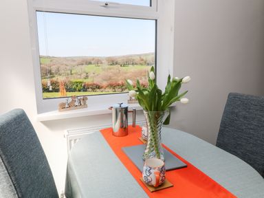 A dining table with a vase of white tulips a coffee pot and mugs by a window showing a countryside view at The View in Cardinham