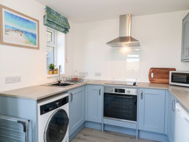 A kitchen with blue cabinets a washing machine an oven a microwave and a cutting board at The View in Cardinham