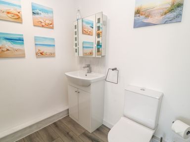 A bathroom with a white sink under a mirrored cabinet and a toilet with photos of the beach on the walls at The View in Cardinham