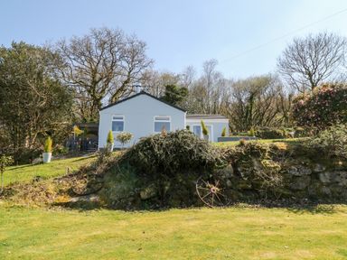 A small white house on a grassy hill with trees and bushes at The View in Cardinham