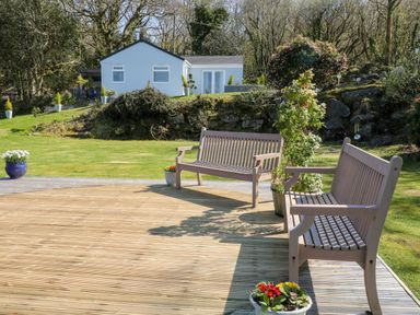 An outdoor deck with two wooden benches and potted plants overlooking a grassy lawn with a white house and trees at The View in Cardinham