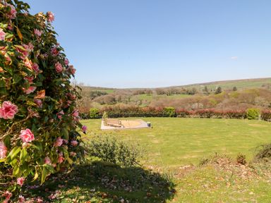 A garden with a wooden bench on a paved circular area and pink flowers in the foreground at The View in Cardinham