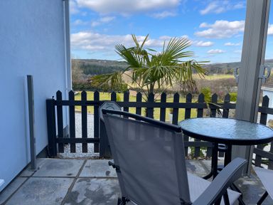 An outdoor patio with a glass table and two chairs next to a black picket fence and a view of a palm tree and countryside at The View in Cardinham