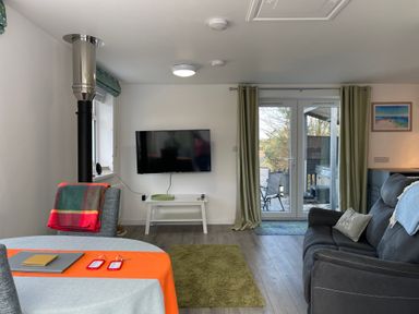 A living room with a TV on the wall a sofa a small table and glass doors leading outside at The View in Cardinham