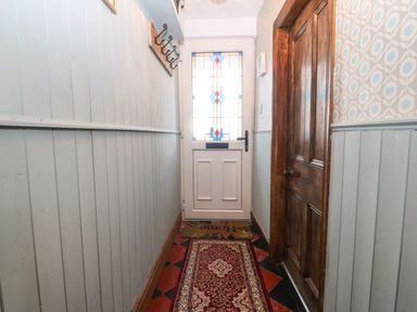 A narrow hallway with a red patterned runner rug a wooden door on the right and a white door with stained glass at the end at Bod Feurig in Penygroes