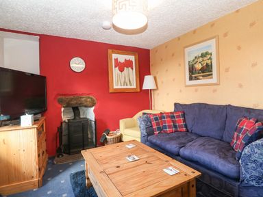 A living room with a blue sofa a wooden coffee table a TV on a wooden stand and a fireplace at Bod Feurig in Penygroes